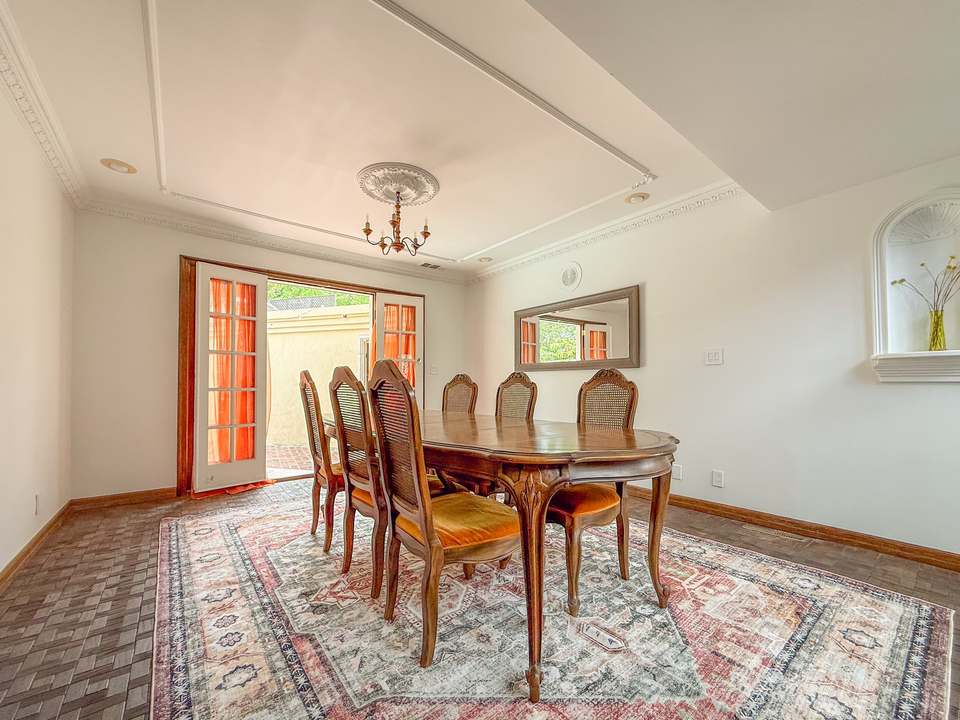 Dining room with a carved wood table, a chandelier and French doors open toward the pool