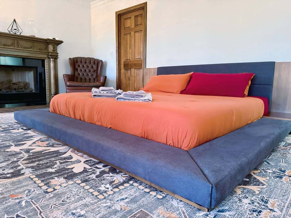 Japanese-inspired low platform king bed with orange bedding beside a fireplace