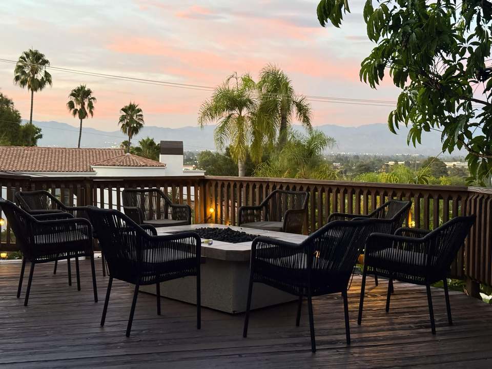 Deck at dusk with a gas fire table ringed by chairs, palm trees and mountains beyond