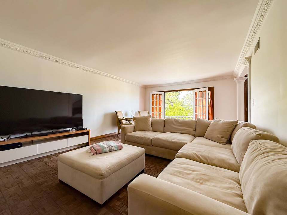 Living room with a beige sectional and ottoman facing a 75-inch TV