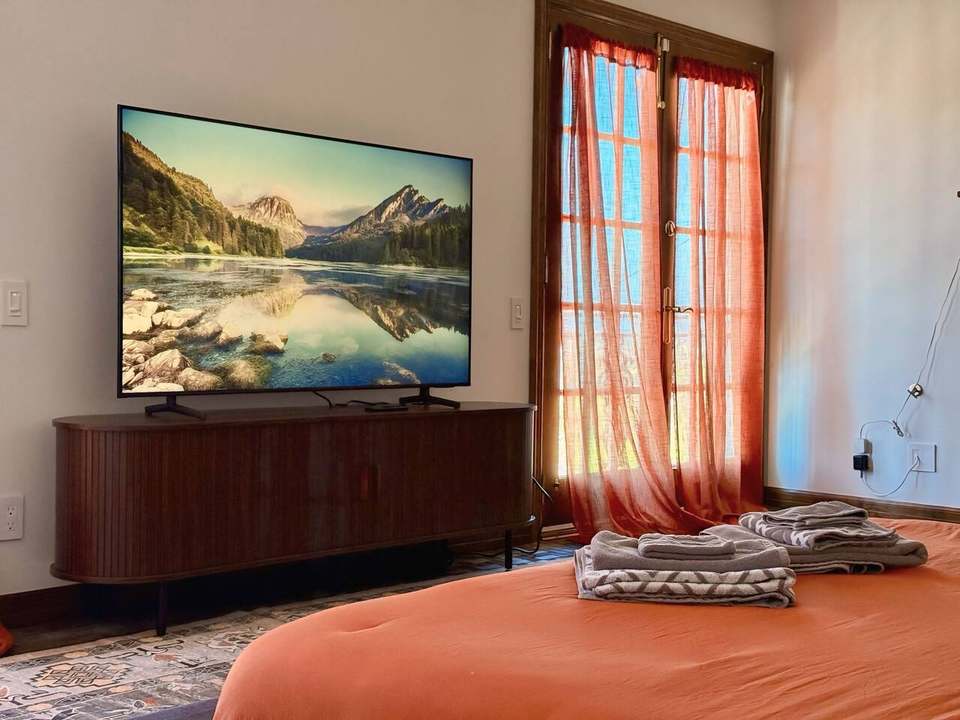 Primary bedroom with a large TV on a wood media console and sheer curtains